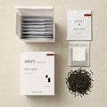 Open DRIFT tea box displaying whole leaf hanging ear sachets in individual sealed pouches